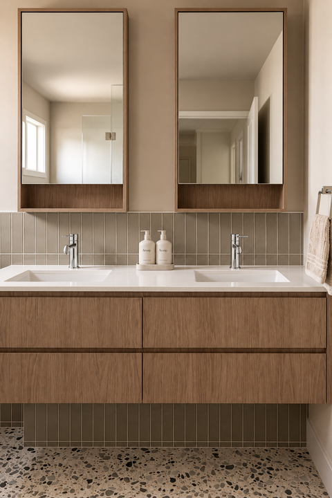 Mitigeur lavabo bas design Mireva chromé Azéo — deux mitigeurs sur une double vasque blanche, meuble suspendu en bois à quatre tiroirs, armoires miroir et sol terrazzo